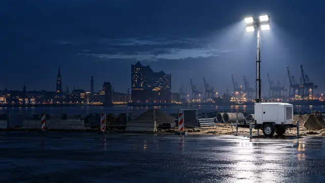 Mobiler Lichtmast auf einer Baustelle am Elbufer, im Hintergrund Elbphilharmonie und Hafenkräne bei Nacht